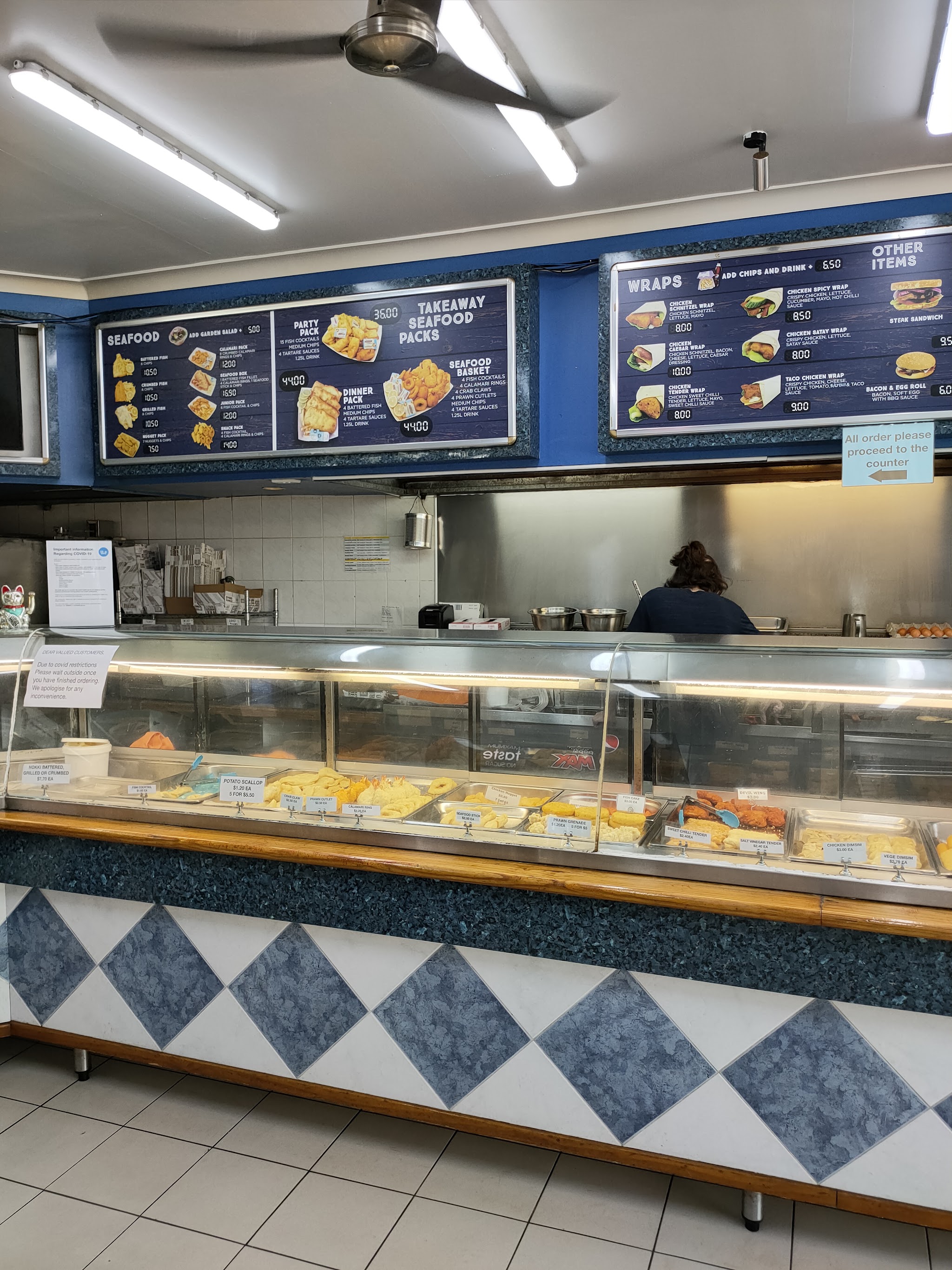 Inside Coona Fish Shop: menu boards above the hot food counter with blue and white diamond tiles